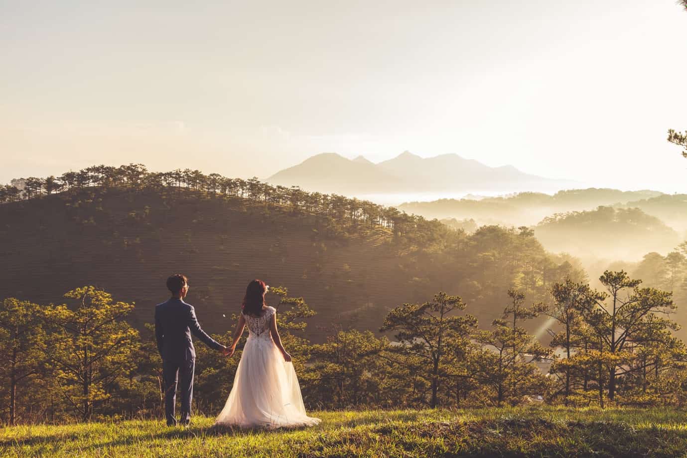 A person and person holding hands and walking in a field with trees and mountains in the background Description automatically generated with medium confidence