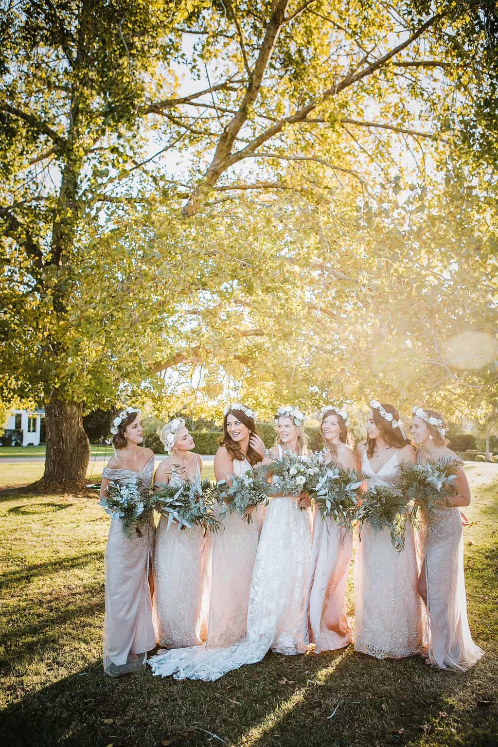 Free Full body of feminine happy young bride and bridesmaids in elegant dresses and floral wreaths holing bouquets of fresh flower while standing together in park on sunny day Stock Photo