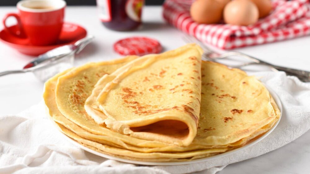 Crepes on a plate on a breakfast table with the last one folder in half.