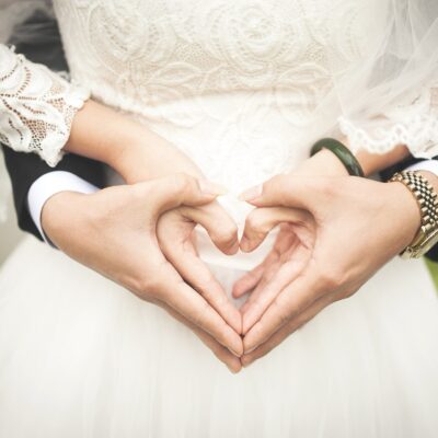 A couple in a wedding dress making a heart with their hands Description automatically generated